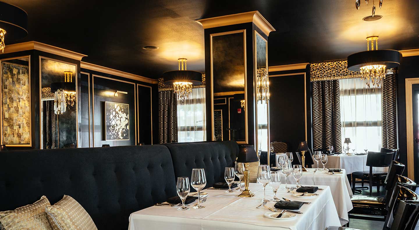 The Bridgeman's Chophouse dining room with white table cloths, rich dark walls with gold accents, and ornate hanging lights