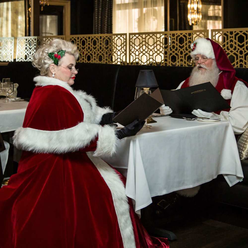 man and woman dressed in santa clothes reading menus at a table